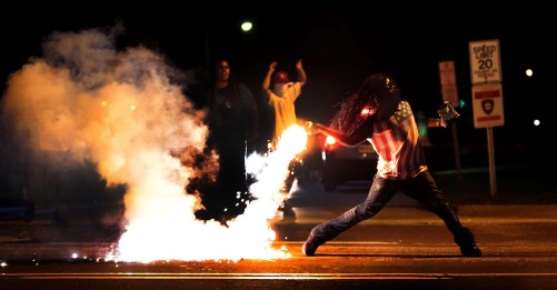 A demonstrator throws back a tear gas container after tactical officers worked to break up a group of bystanders in Ferguson, Aug. 13. (Robert Cohen/St. Louis Post-Dispatch)
